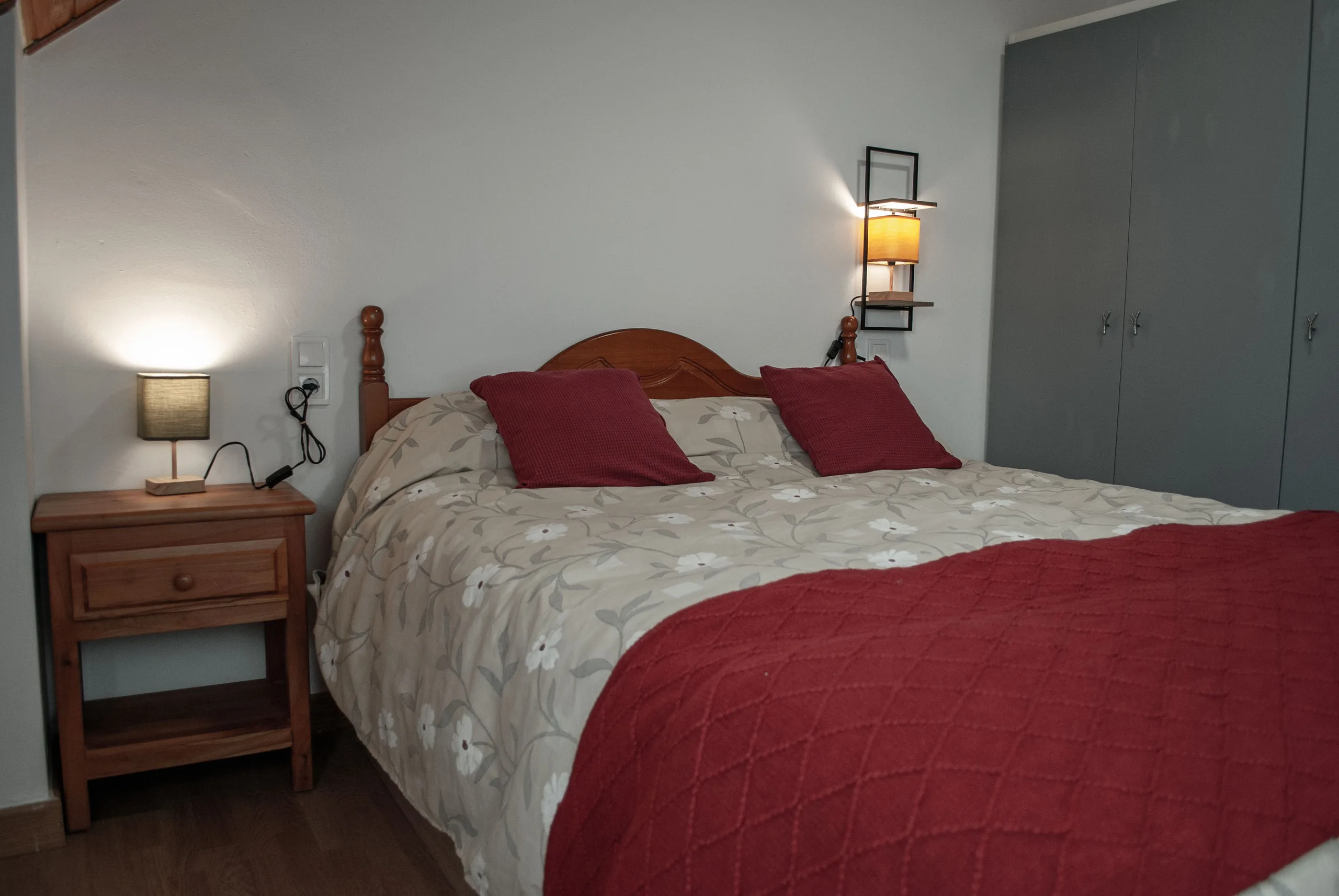 Dormitorio principal con cama de matrimonio, colcha granate y lámparas de noche