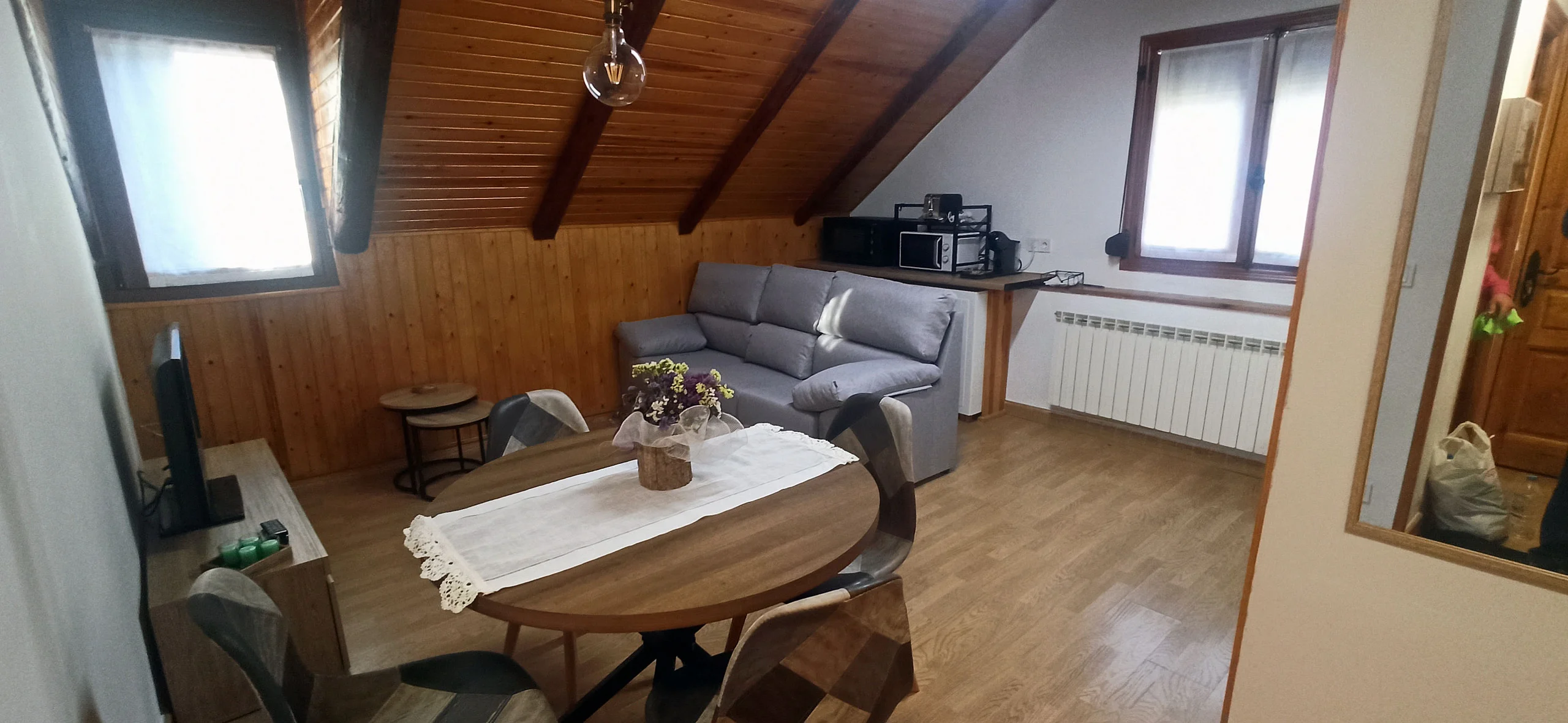Zona de estar abuhardillada con sofá, mesa y el techo de madera a la vista